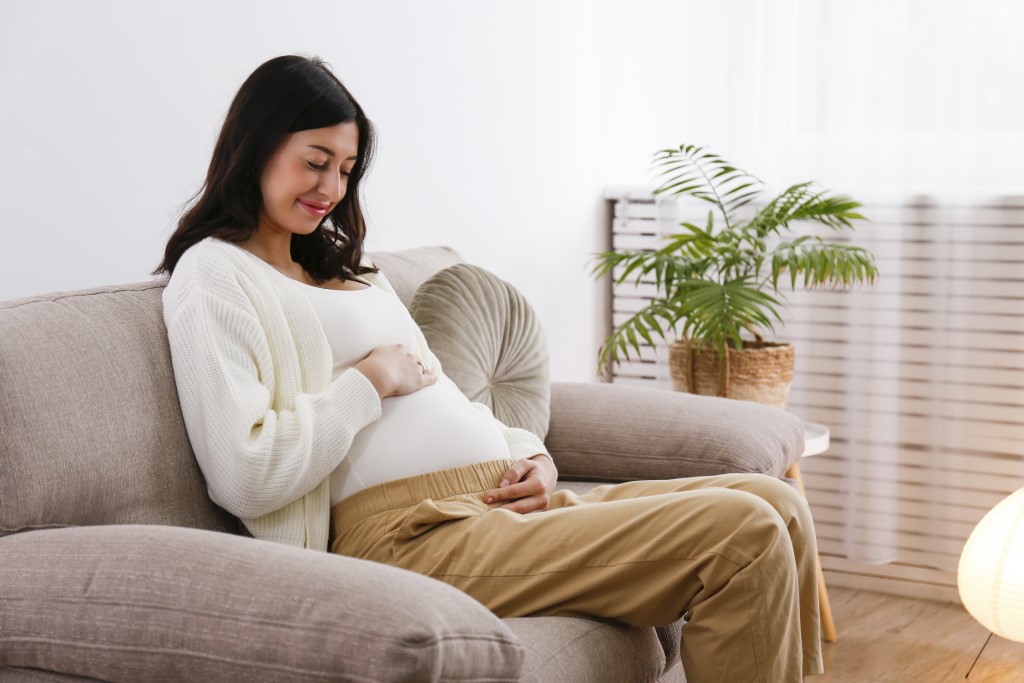 Young beautiful pregnant woman on second trimester of pregnancy sitting on the couch of doctor's office waiting for checkup. Regular prenatal care visit concept. Background, copy space, close up